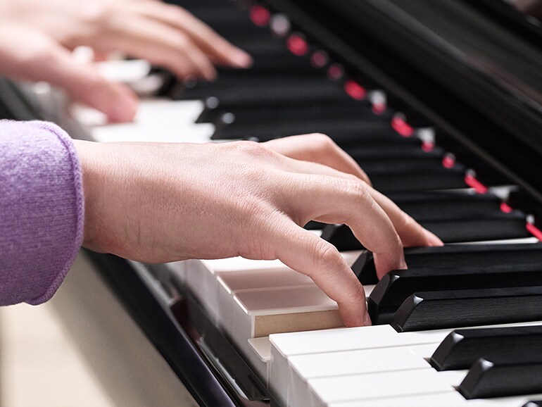 Hands playing wooden-key GrandTouch-S keys on a Yamaha Clavinova, as on the CLP-845